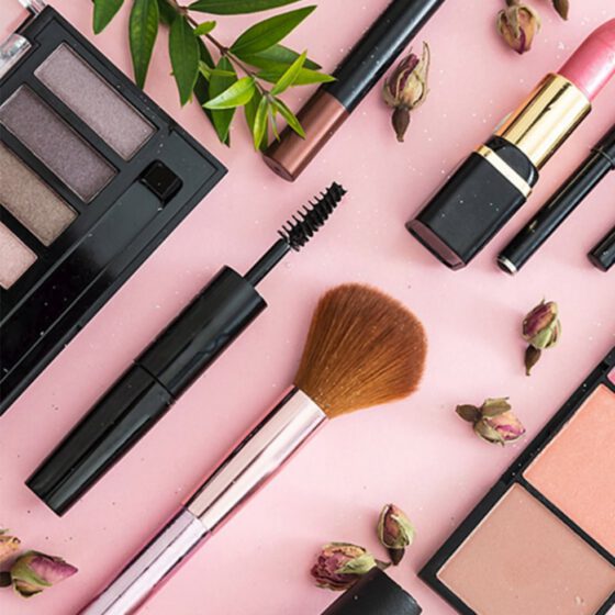 Viasun cosmetics displayed with makeup brushes and lipsticks on pink background.